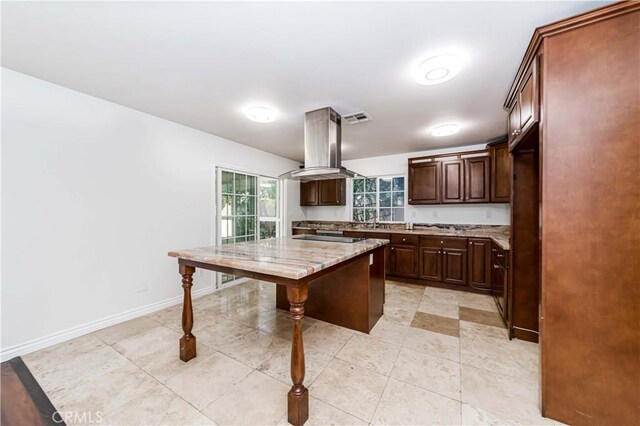 kitchen with dark brown cabinetry, a kitchen island, island exhaust hood, black electric stovetop, and light stone countertops