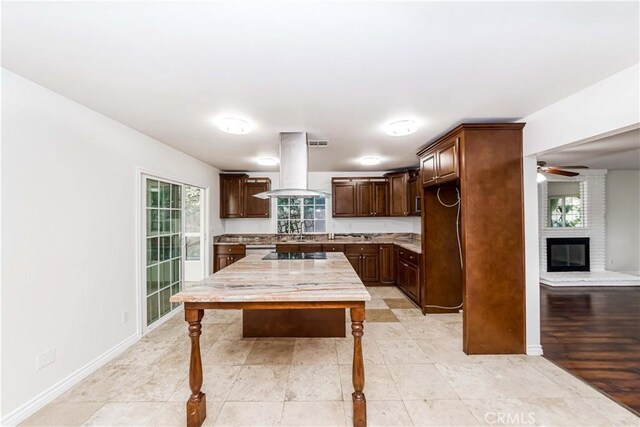 kitchen featuring sink, island range hood, a brick fireplace, dark brown cabinets, and black electric stovetop