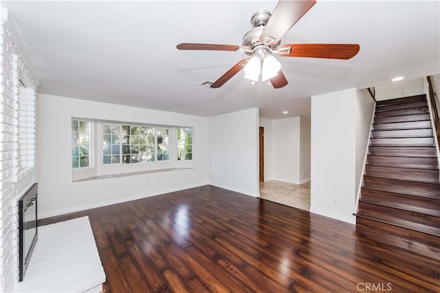 unfurnished living room featuring wood finished floors, visible vents, baseboards, stairway, and a brick fireplace