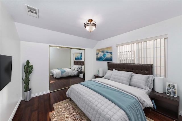 bedroom featuring lofted ceiling, wood finished floors, visible vents, baseboards, and a closet