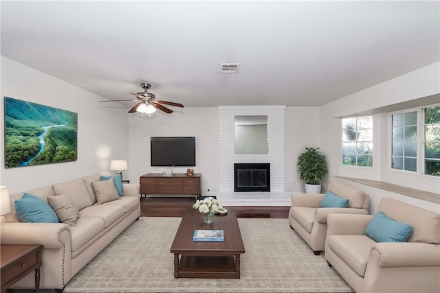 living room featuring ceiling fan, a fireplace, wood finished floors, and visible vents