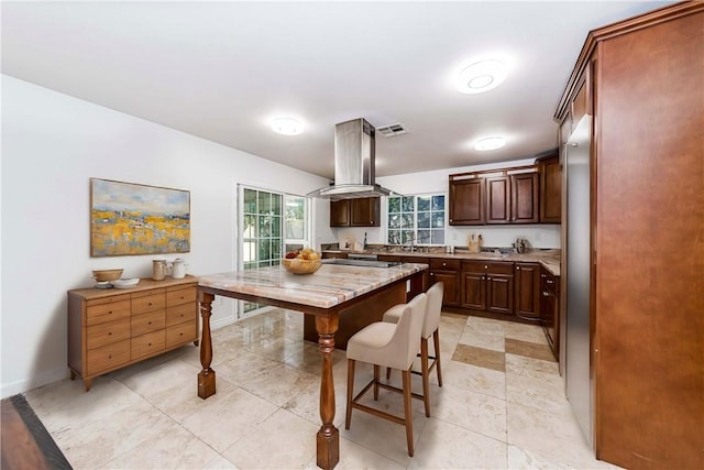 kitchen featuring visible vents, island range hood, baseboards, light stone countertops, and dark brown cabinets