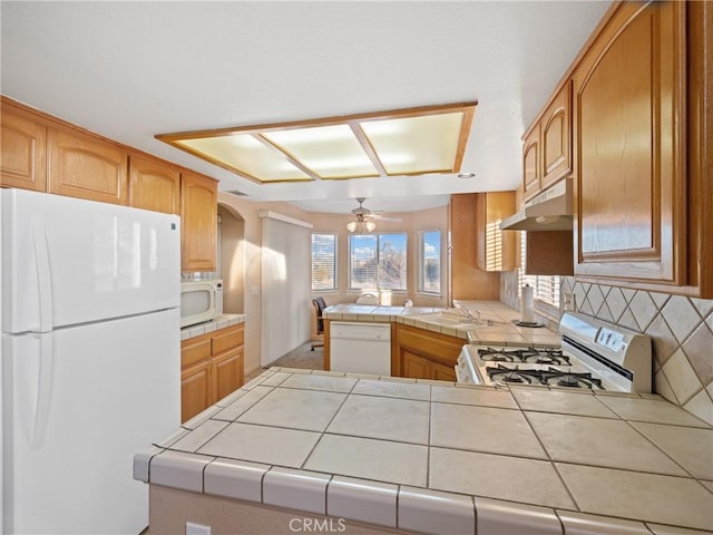 kitchen with white appliances, tile countertops, kitchen peninsula, and ceiling fan