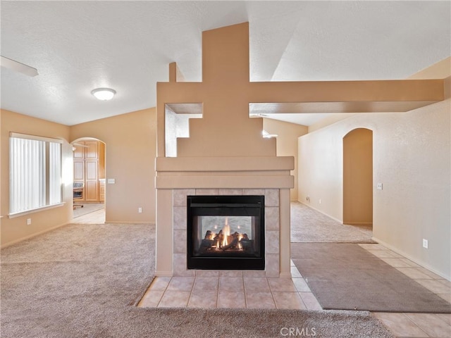 unfurnished living room with light colored carpet, a tiled fireplace, and vaulted ceiling