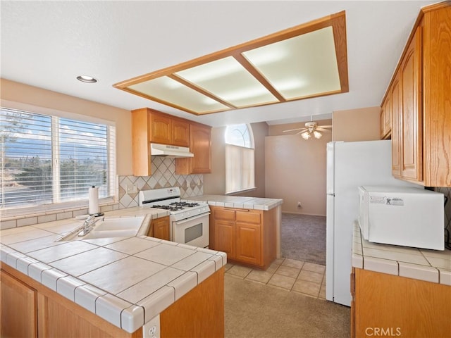 kitchen featuring white range with gas cooktop, tile counters, light colored carpet, and kitchen peninsula