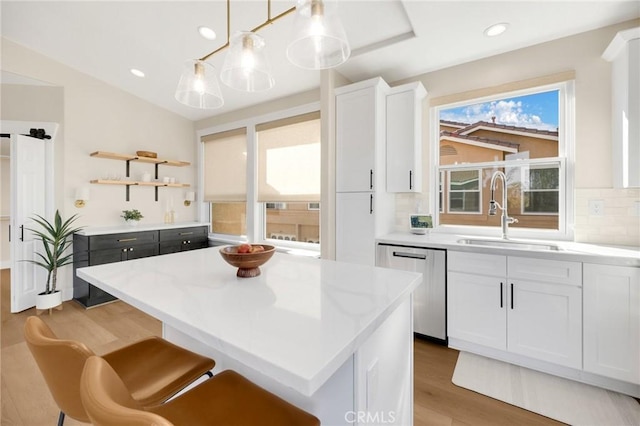 kitchen with sink, white cabinetry, decorative light fixtures, dishwasher, and a kitchen island