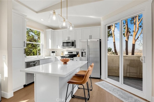 kitchen with white cabinetry, a center island, light wood-type flooring, appliances with stainless steel finishes, and backsplash