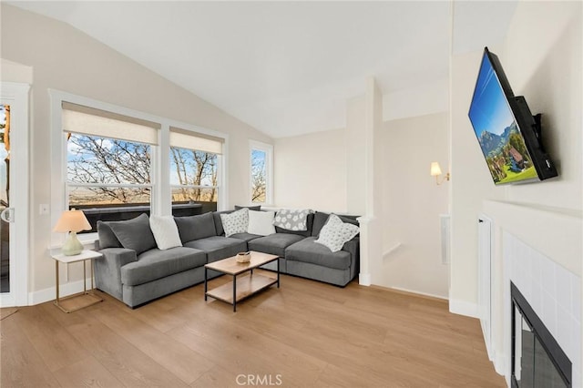 living room with a tiled fireplace, vaulted ceiling, and light hardwood / wood-style floors