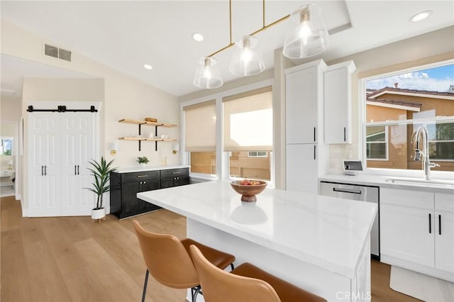 kitchen with hanging light fixtures, dishwasher, a barn door, and white cabinets