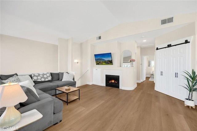 living room with lofted ceiling, a barn door, and light wood-type flooring