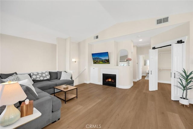 living room with a barn door, vaulted ceiling, and light wood-type flooring