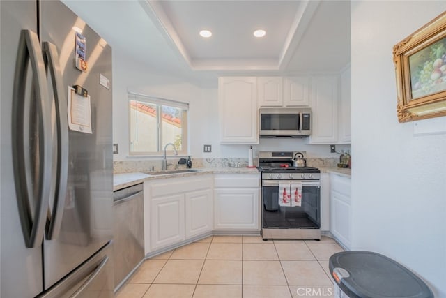 kitchen featuring appliances with stainless steel finishes, sink, white cabinets, light tile patterned floors, and a raised ceiling