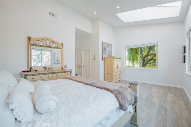 bedroom featuring a skylight, light hardwood / wood-style flooring, and a high ceiling