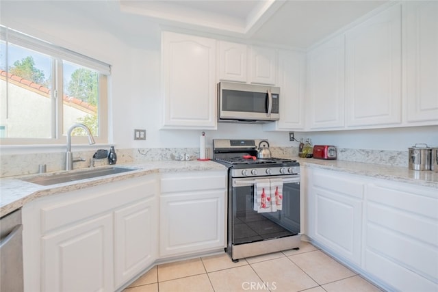 kitchen featuring light tile patterned flooring, sink, white cabinetry, light stone counters, and appliances with stainless steel finishes