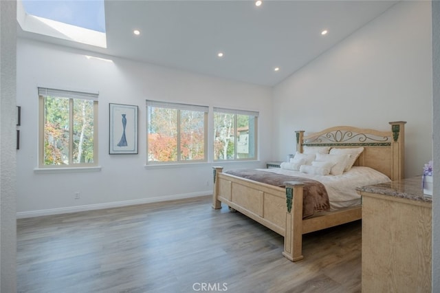 bedroom with hardwood / wood-style flooring, a skylight, and high vaulted ceiling