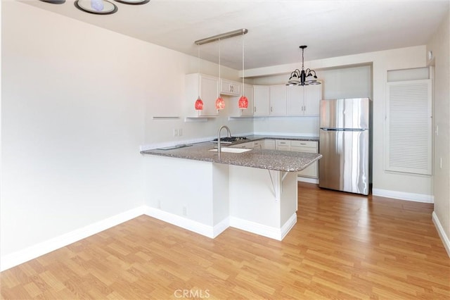 kitchen with pendant lighting, light hardwood / wood-style floors, stainless steel refrigerator, and kitchen peninsula