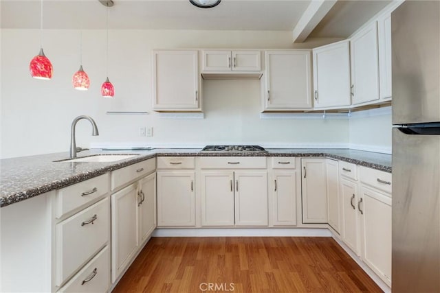 kitchen with decorative light fixtures, sink, white cabinets, stainless steel appliances, and light hardwood / wood-style flooring