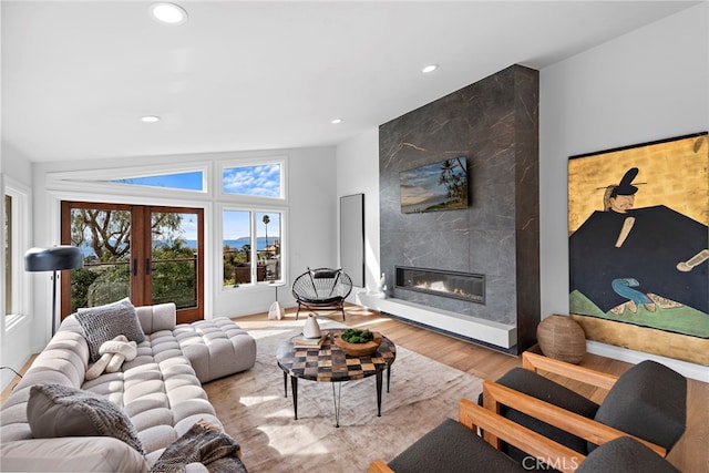 living room featuring wood finished floors, recessed lighting, vaulted ceiling, french doors, and a large fireplace