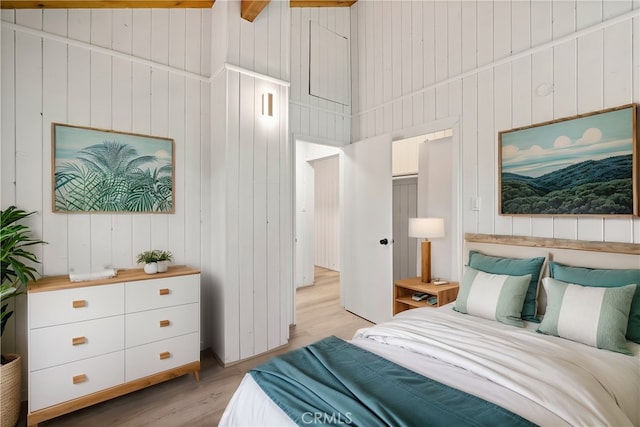 bedroom featuring vaulted ceiling, wood walls, and light wood-type flooring