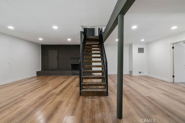 basement featuring a brick fireplace and light hardwood / wood-style flooring