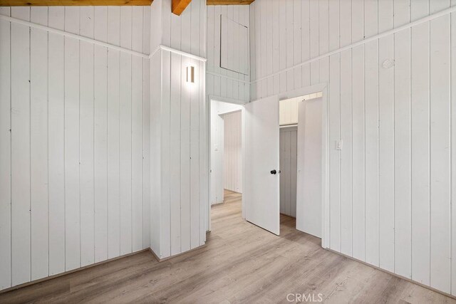 spare room featuring wooden walls, lofted ceiling with beams, and light wood-type flooring