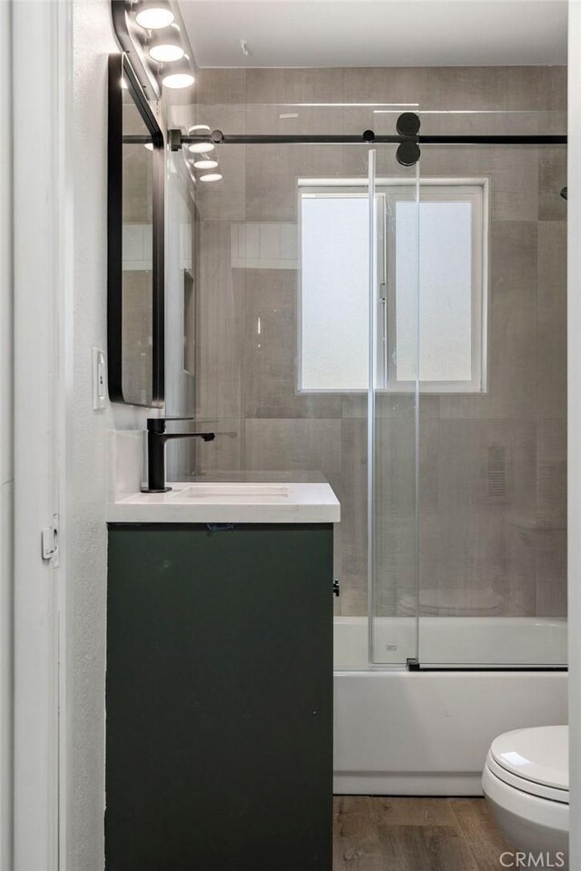 full bathroom featuring vanity, toilet, hardwood / wood-style floors, and combined bath / shower with glass door