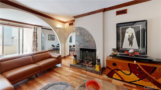 living room with a tiled fireplace, wood-type flooring, and ornamental molding