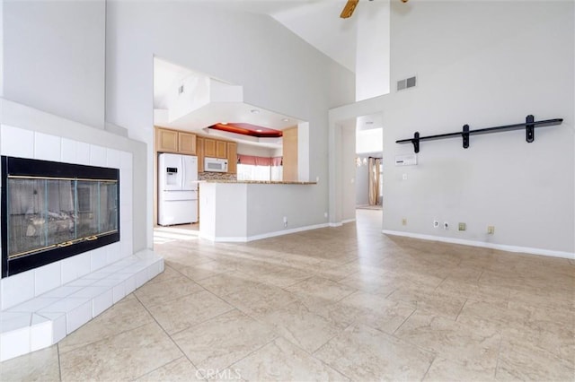 unfurnished living room with a barn door, ceiling fan, a fireplace, and high vaulted ceiling