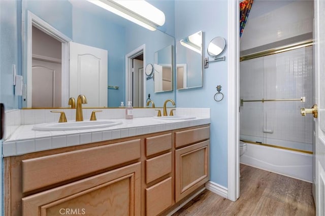 full bathroom featuring hardwood / wood-style flooring, bath / shower combo with glass door, vanity, and toilet