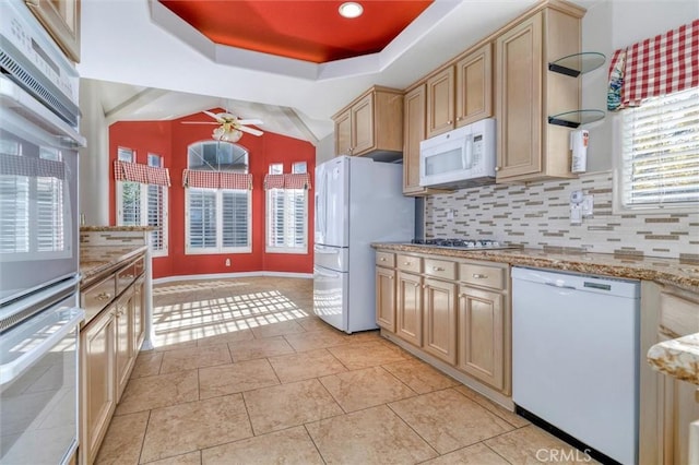 kitchen with white appliances, ceiling fan, light brown cabinetry, decorative backsplash, and a raised ceiling