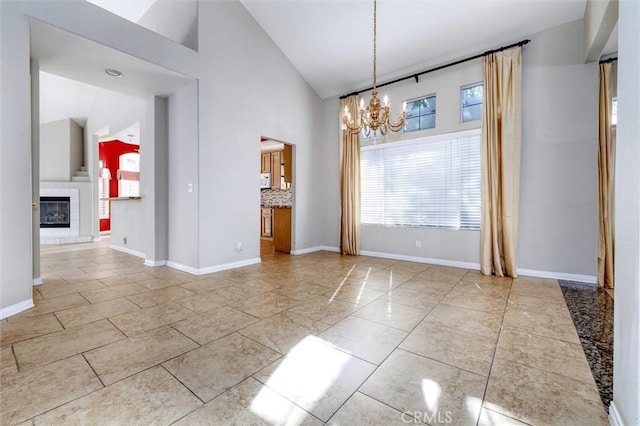 unfurnished dining area with a healthy amount of sunlight, high vaulted ceiling, a tile fireplace, and a notable chandelier