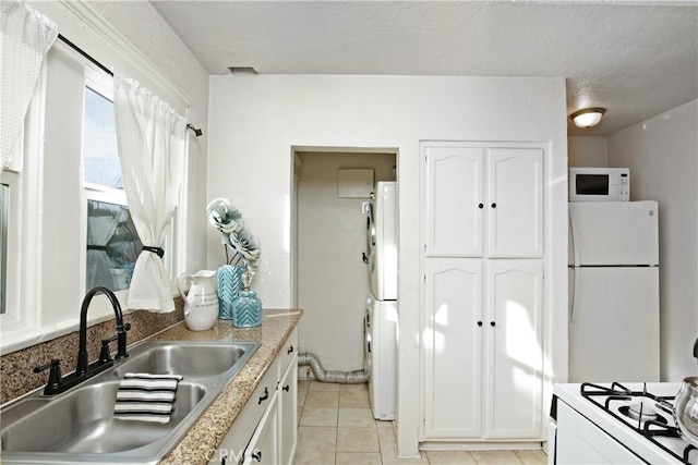 kitchen with stacked washer and clothes dryer, light countertops, white cabinetry, a sink, and white appliances