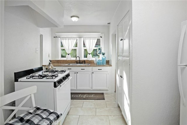 kitchen featuring light tile patterned floors, white gas range, a textured wall, white cabinets, and a sink