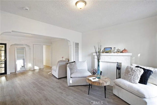 living area with arched walkways, a textured ceiling, a fireplace, wood finished floors, and ornamental molding