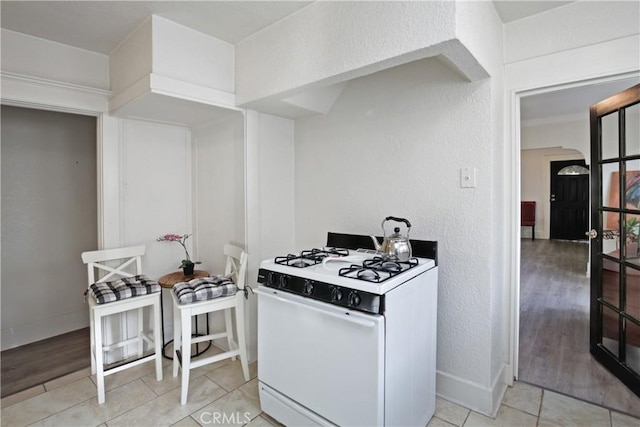 kitchen with arched walkways, a textured wall, light tile patterned flooring, baseboards, and white gas range oven