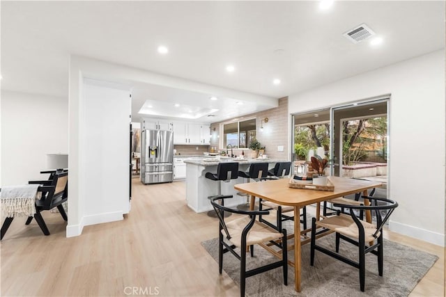 dining room with sink, a raised ceiling, and light hardwood / wood-style floors