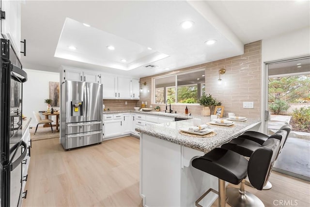 kitchen featuring a kitchen breakfast bar, stainless steel refrigerator with ice dispenser, kitchen peninsula, white cabinets, and a raised ceiling