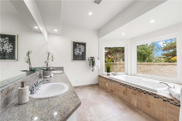 bathroom with a relaxing tiled tub, vanity, and tile patterned floors