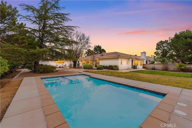 pool at dusk featuring a patio area and a lawn