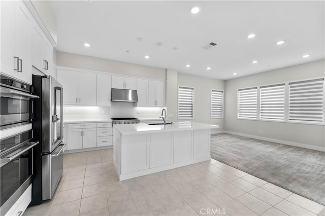 kitchen with an island with sink, sink, light carpet, and white cabinets