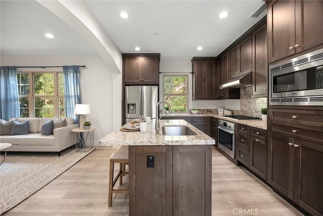 kitchen with sink, a breakfast bar, appliances with stainless steel finishes, dark brown cabinetry, and a center island with sink