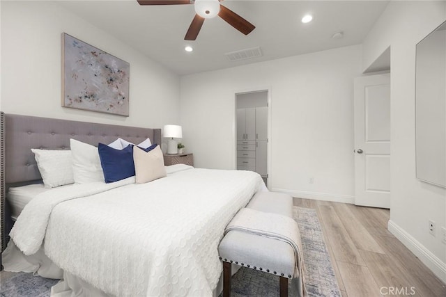 bedroom featuring a walk in closet, a closet, ceiling fan, and light wood-type flooring