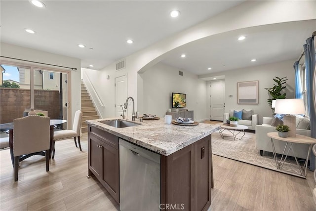 kitchen with dark brown cabinetry, sink, a center island with sink, light wood-type flooring, and dishwasher