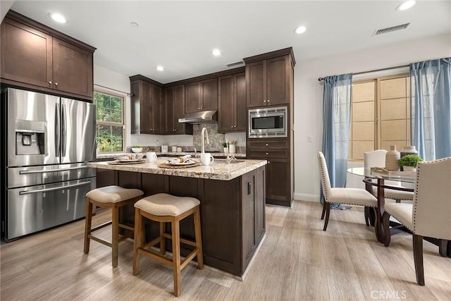 kitchen featuring a kitchen island, light stone countertops, appliances with stainless steel finishes, and light hardwood / wood-style floors