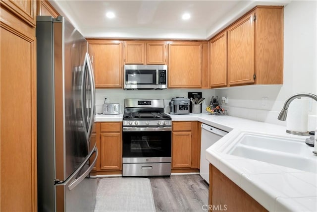 kitchen featuring stainless steel appliances, tile counters, sink, and light wood-type flooring