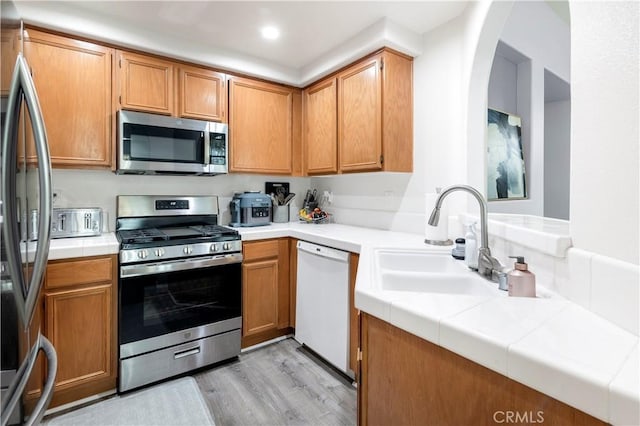 kitchen featuring sink, light hardwood / wood-style flooring, stainless steel appliances, and tile countertops