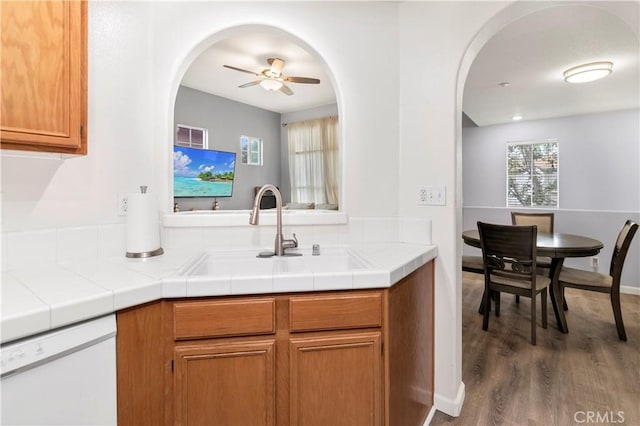 kitchen featuring dark wood-type flooring, sink, tile countertops, dishwasher, and ceiling fan