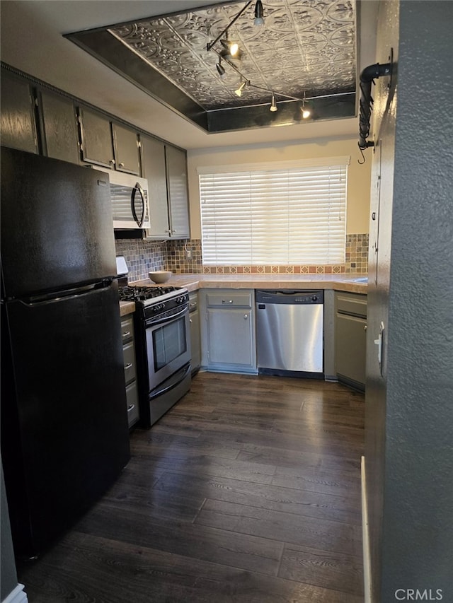 kitchen with gray cabinets, appliances with stainless steel finishes, backsplash, dark hardwood / wood-style floors, and a tray ceiling