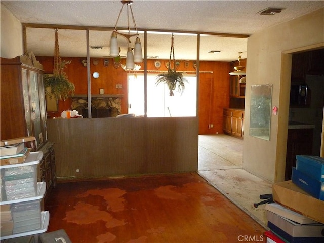 kitchen featuring hanging light fixtures, concrete flooring, a textured ceiling, and wooden walls