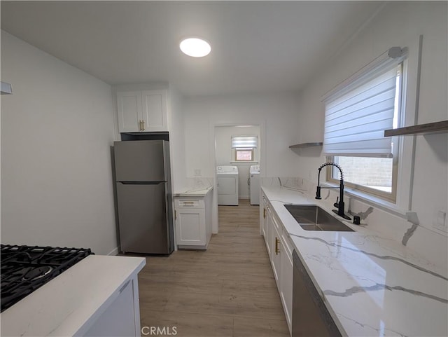 kitchen featuring sink, white cabinetry, stainless steel refrigerator, light stone countertops, and washer and clothes dryer